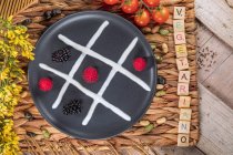 Top view of noughts and cross game concept on plate with fresh blackberries and raspberries between whipped cream near inscription — стоковое фото