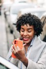 Alto angolo di sorridente donna afroamericana con acconciatura riccia labbra rouging con rossetto in piedi vicino auto in ingorgo traffico — Foto stock