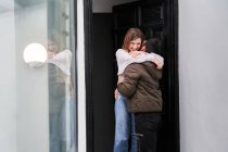 Cheerful young lady meeting anonymous boyfriend with luggage returned from business trip on doorstep of house while hugging — Stock Photo