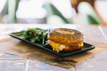 Appetitliches Bagel-Sandwich mit Käse und Huhn auf Teller serviert mit Rucola-Salat auf dem Tisch im Café — Stockfoto