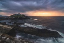 Breathtaking scenery of rocky island with lighthouse located in ocean near rocky coast in Faro Tapia de Casariego in Asturias in Spain under cloudy sky at sunrise — Stock Photo
