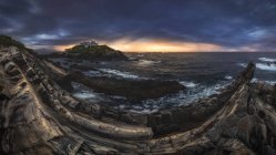 Impresionante paisaje de isla rocosa con faro situado en el océano cerca de costa rocosa en Faro Tapia de Casariego en Asturias en España bajo cielo nublado al amanecer - foto de stock