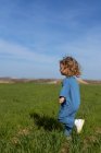 Vue latérale de la fille ravie avec les cheveux bouclés souriant et courant sur l'herbe verte contre le ciel bleu le jour d'été dans le champ — Photo de stock