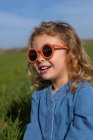 Linda niña feliz en ropa de moda y gafas de sol sentado y relajante en el césped cubierto de hierba - foto de stock