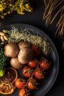 Vista dall'alto del piatto con mazzetto di pomodorini freschi vicino patate cotte e germogli su sfondo grigio con fiori — Foto stock