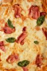 Крупный план вкусной домашней пиццы с базиликом и ветчиной, подаваемой на столе — стоковое фото