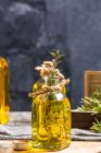 Botella de vidrio de aceite esencial con ramitas de romero y vela de madera orgánica en la mesa gris - foto de stock