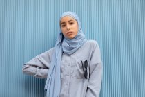 Jeune femme musulmane solitaire au regard mélancolique regardant la caméra contre un mur nervuré pendant la journée — Photo de stock