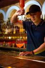 Giovane barista asiatico che versa succo di pompelmo nel bicchiere mentre prepara un cocktail nel bar — Foto stock