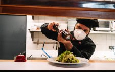 Chef masculino serio trabajando en cocina de restaurante y añadiendo condimentos en plato en plato - foto de stock