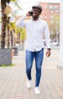 Trendy African American male walking on street with palm trees and talking mobile phone — Stock Photo