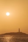 Картинний краєвид хвилястої води океану, що промиває узбережжя з високогірним маяком, поміщеним у Фаро - де - Трафальгар (Кадіс, Іспанія) під яскравим оранжевим небом на світанку. — стокове фото