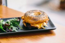 Апетитна бутерброд з сиром і куркою, подається на тарілці з салатом рукола на столі в кафе — стокове фото