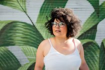 Content adult overweight female in eyewear curly hair against ornamental wall in daytime — Stock Photo