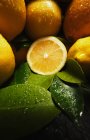 Аппетитные свежие сочные апельсины и лимон с капельками воды и зелеными листьями — стоковое фото