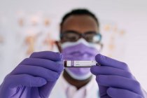 Afroamerikanischer Arzt im Medizinhandschuh demonstriert Reagenzglas mit Blutprobe auf weißem Hintergrund — Stockfoto