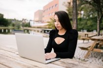 Сосредоточенная женщина-предприниматель сидит за столом с ноутбуком в парке и работает удаленно — стоковое фото