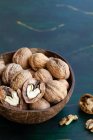 Round shaped wooden bowl full of crunchy walnuts with dry uneven nutshells on table — Stock Photo