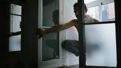 Pensive male sitting on knees on windowsill at home — Stock Photo