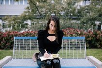 Elegante imprenditrice seduta sulla panchina e che prende appunti nell'organizzatore mentre lavora nel parco urbano — Foto stock