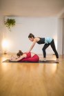 Vista laterale del coltivatore donna istruttore sostenere donna nel fare seduto curva in avanti durante l'allenamento di yoga sul tappeto sportivo in studio — Foto stock