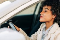 Vista laterale del driver femminile afroamericano allegro in abito alla moda sorridente durante la guida di un'automobile moderna per strada — Foto stock