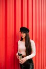 Empresária confiante em roupas da moda em pé com bebida para ir à cidade no fundo da parede vermelha e olhando para longe — Fotografia de Stock