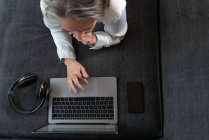 Visão superior da cultura anônimo feminino distância trabalhador navegar internet no netbook no sofá com fone de ouvido sem fio em casa — Fotografia de Stock