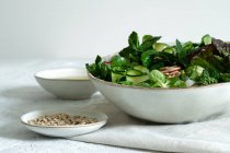 Ensalada de verduras frescas y saludables en un tazón servido sobre la mesa con aceite de oliva y semillas de girasol - foto de stock