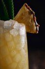 Mesa de madeira com copo de coquetel amarelo com cubos de gelo e coquetel refrescante decorado com folhas pontiagudas e palha listrada — Fotografia de Stock