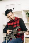 Adult professional bearded male musician playing bass guitar during rehearsal against shelves at home — Stock Photo