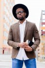African American male in stylish hat and jacket standing on city street and holding book — Stock Photo