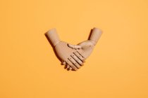 Top view of wooden hands demonstrating handshake as sign of agreement placed on yellow background — Stock Photo