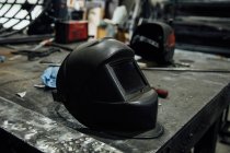 Table en métal avec masque de soudage près de la bobine de papeterie avec fil électrique dans le garage professionnel — Photo de stock