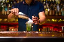 Barman irreconhecível derramando gelo esmagado no copo enquanto prepara coquetel de mojito no bar — Fotografia de Stock