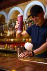 Молодой азиатский бармен наливает клубничный сок в шейкер во время приготовления коктейля в баре — стоковое фото