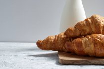 Deliciosos croissants y botella de leche puesta en la mesa para el desayuno en la cocina - foto de stock