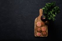 Draufsicht auf frische reife, in Scheiben geschnittene schwarze Tomaten und grüne Minzstiele auf einem Holzschneidebrett auf schwarzem Hintergrund — Stockfoto