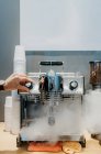 Cultiver barista anonyme en utilisant mousseur de lait tout en nettoyant la machine à café à la cafétéria pendant le travail de jour — Photo de stock