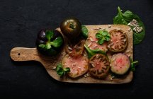 Vue du dessus de tomates noires fraîches mûres tranchées et de tiges de menthe verte sur planche à découper en bois sur fond noir — Photo de stock