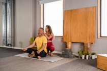Концентрована жінка-тренер в спортивному одязі навчає чоловіка медитувати позу під час йоги сесії в студії — стокове фото