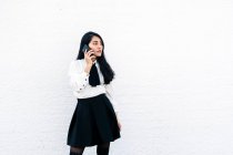 Підлітки - жінки з Азії формально стоять біля білої стіни і розмовляють по мобільному телефону. — стокове фото