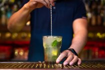 Barman irreconhecível segurando o copo e mexendo coquetel de mojito no bar — Fotografia de Stock