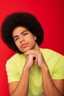 Young self confident African American male in casual t shirt leaning on hands looking at camera on red background — Stock Photo
