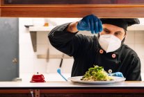 Chefe masculino sério que trabalha na cozinha do restaurante e acrescenta o sal no prato na chapa — Fotografia de Stock