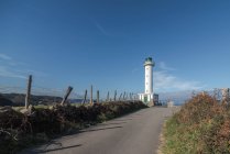Estrada de asfalto que leva ao farol branco colocado em Faro de Lastres, nas Astúrias, em Espanha, sob céu azul sem nuvens durante o dia — Fotografia de Stock