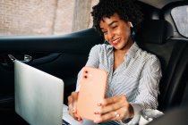 Mulher afro-americana alegre sorrindo e tirando selfie com telefone celular no automóvel moderno — Fotografia de Stock