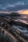 Paesaggio mozzafiato di isola rocciosa con faro situato nell'oceano vicino alla costa rocciosa a Faro Tapia de Casariego nelle Asturie in Spagna sotto il cielo nuvoloso all'alba — Foto stock