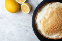 Вид на аппетитный пирог с безе, подаваемый на мраморном столе со свежими лимонами на кухне — стоковое фото
