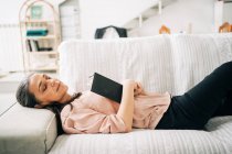 Зверху сонна жінка середнього віку лежить на зручному дивані з пледом під час відпочинку у вітальні вдома — стокове фото